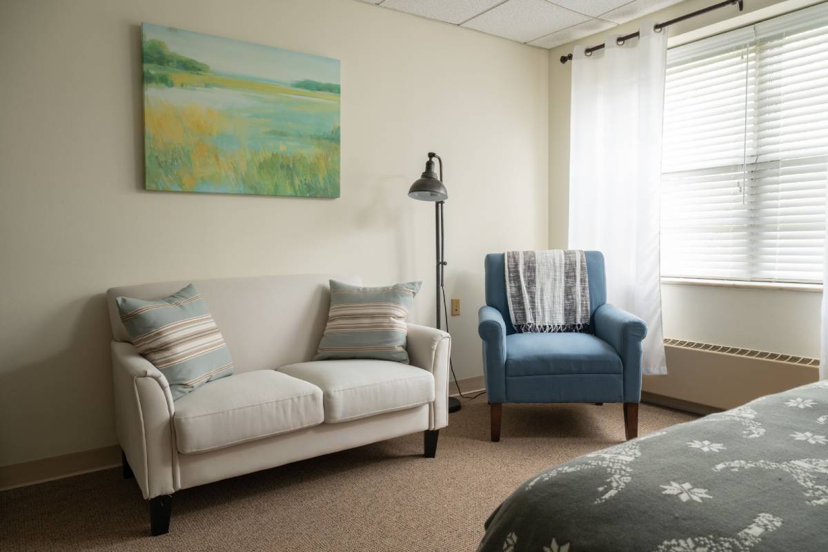 itman Manor apartment living area with sofa, blue accent chair and large window.