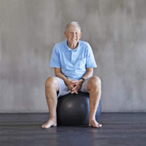 Shot of an elderly man using weights while sitting on a swiss ball