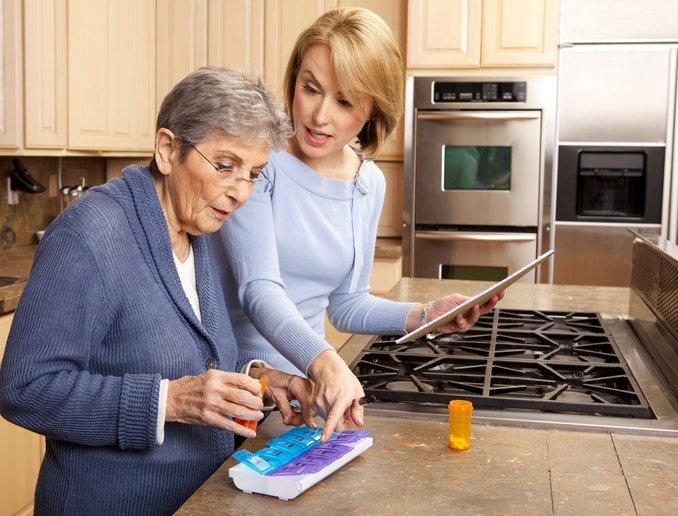 Caregiver assisting senior woman sort out her medication
