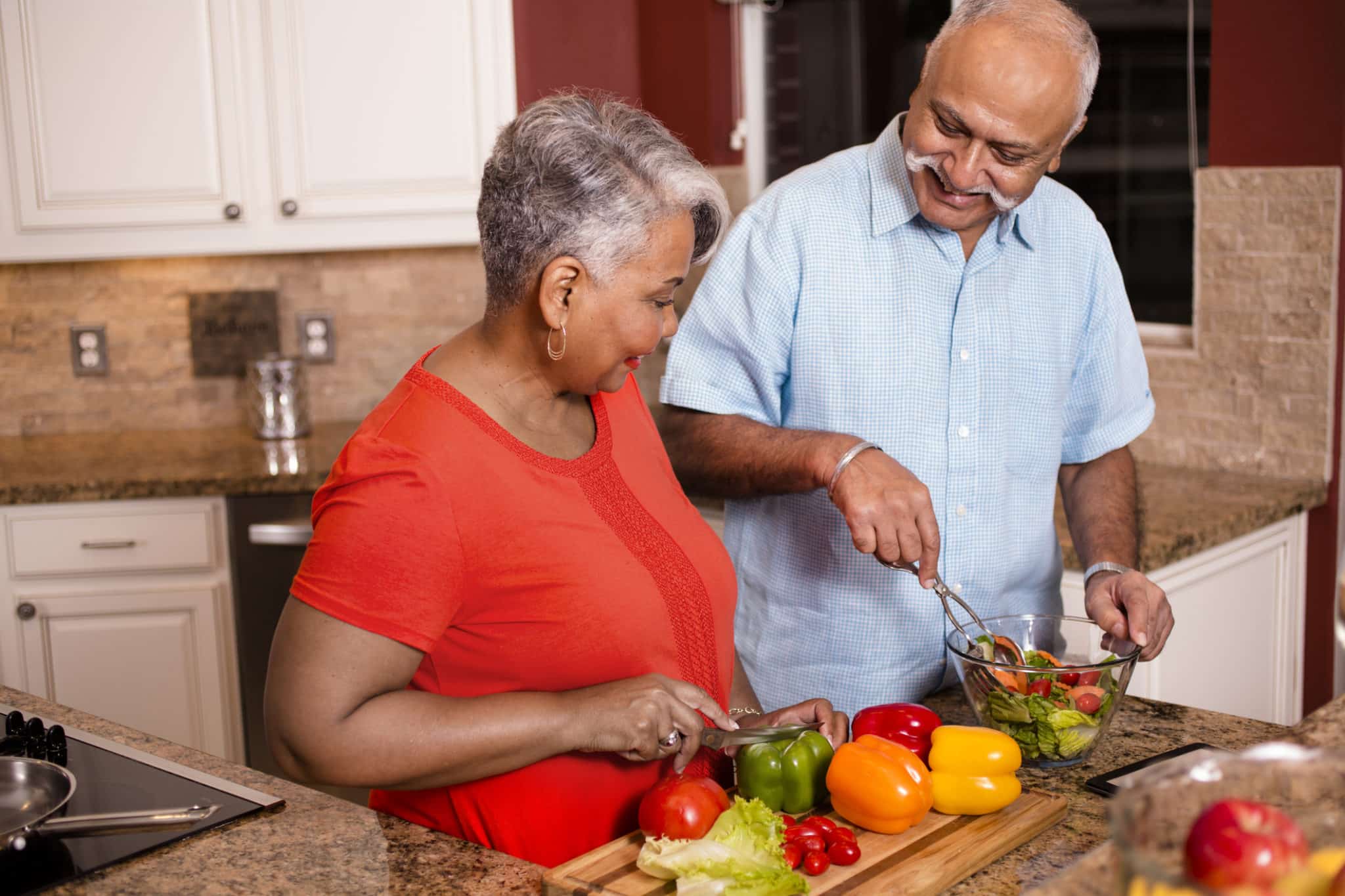 Happy senior adult couple cooking together in home kitchen.