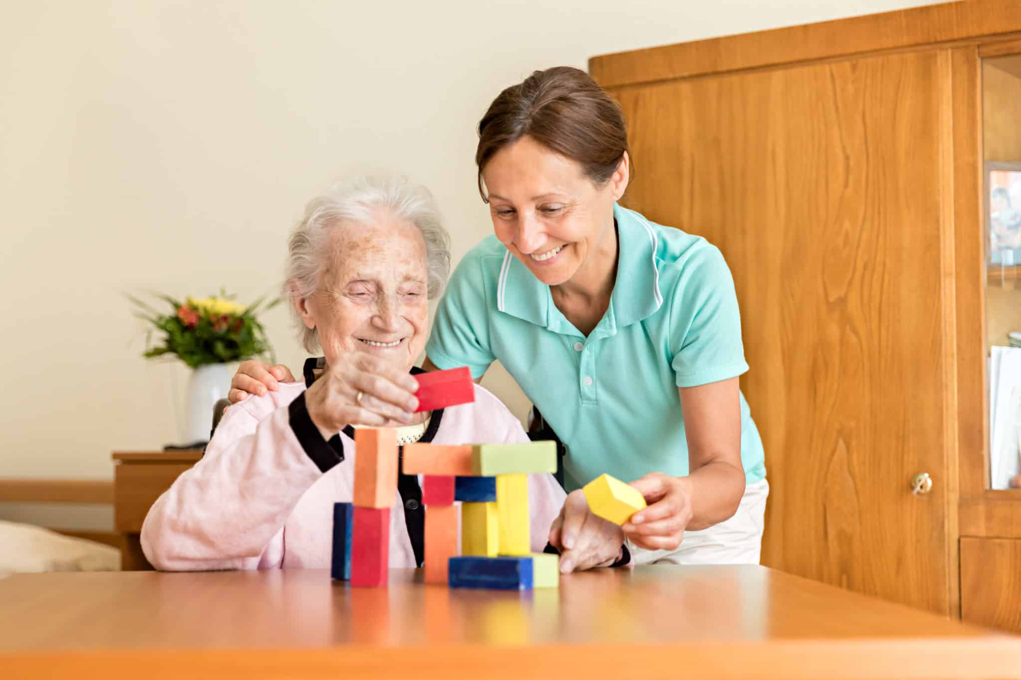 Dementia and Occupational Therapy - Home caregiver and senior adult woman playing with blocks