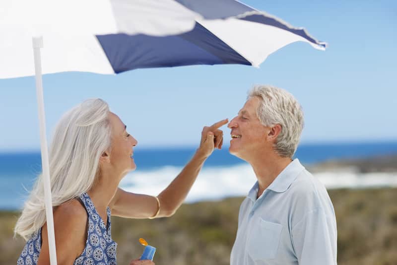 Senior woman applying sunscreen to mans nose