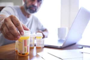 Hispanic Man Sitting At Dining Room Table Reaches For His Prescription Medications
