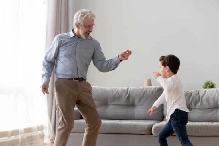 Happy grandfather and little grandchild dancing to music together