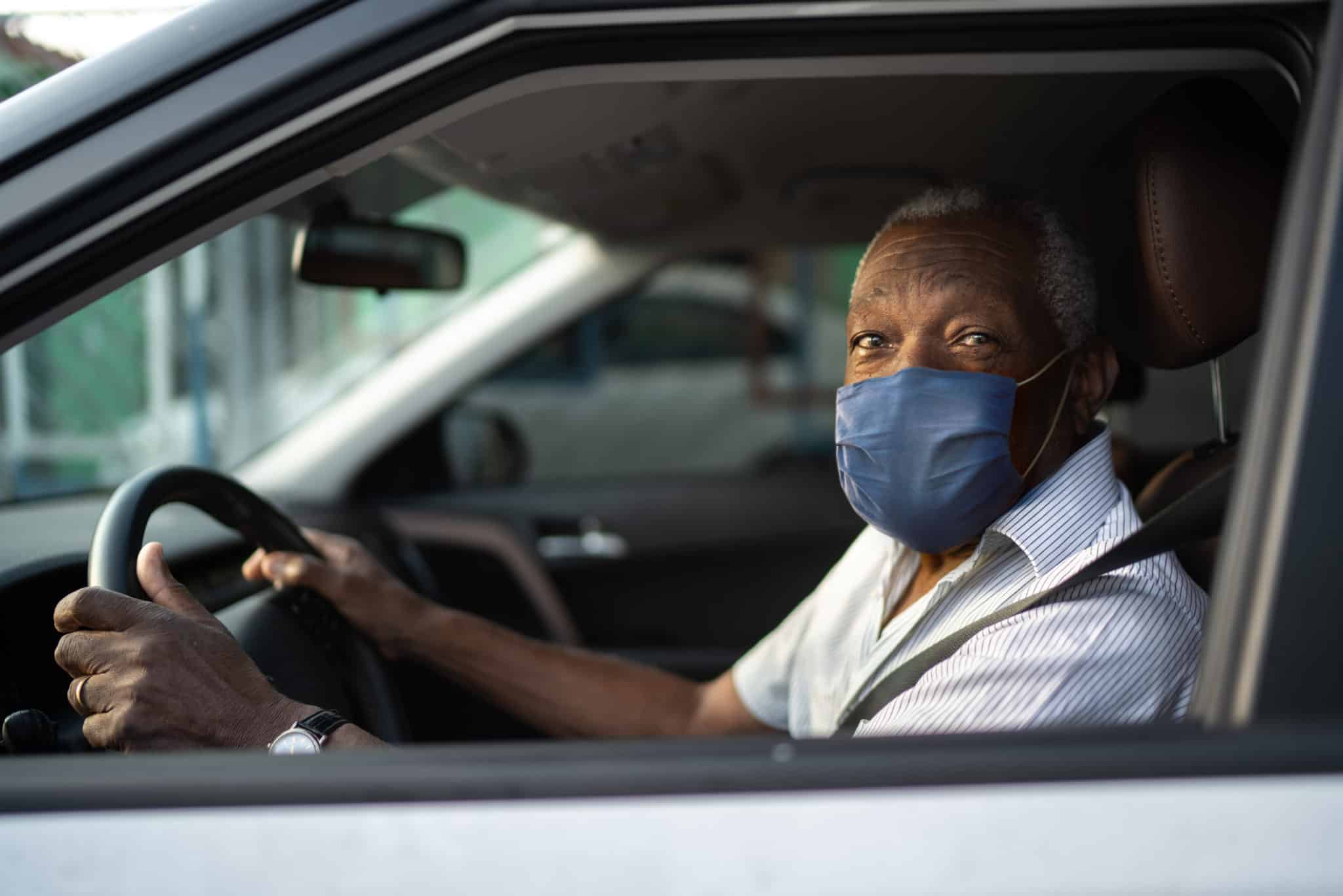 Portrait of senior african man driving a car with face mask