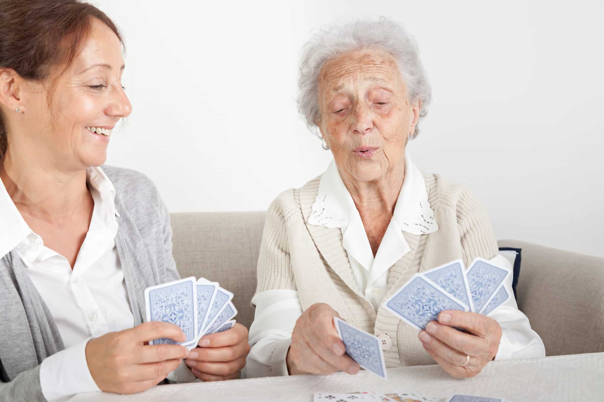 Senior woman with her home caregiver playing cards