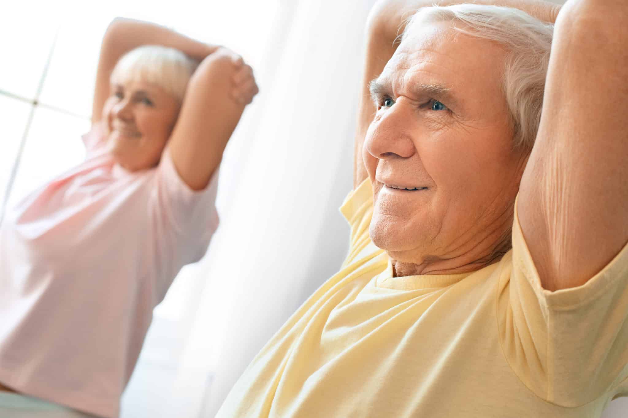 Senior couple exercise together at home health care shoulder stretching