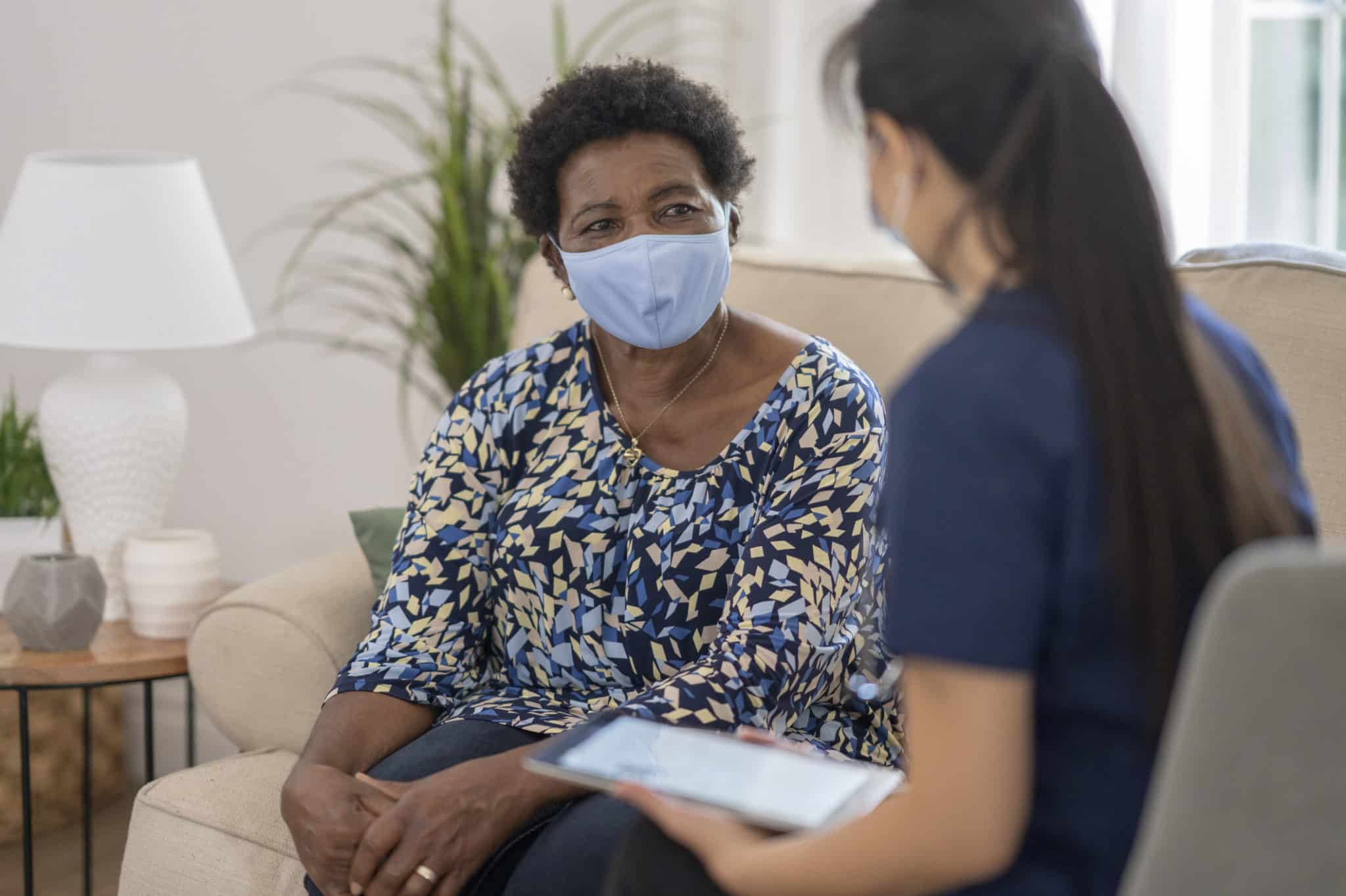 Home caregiver visiting with patient wearing masks