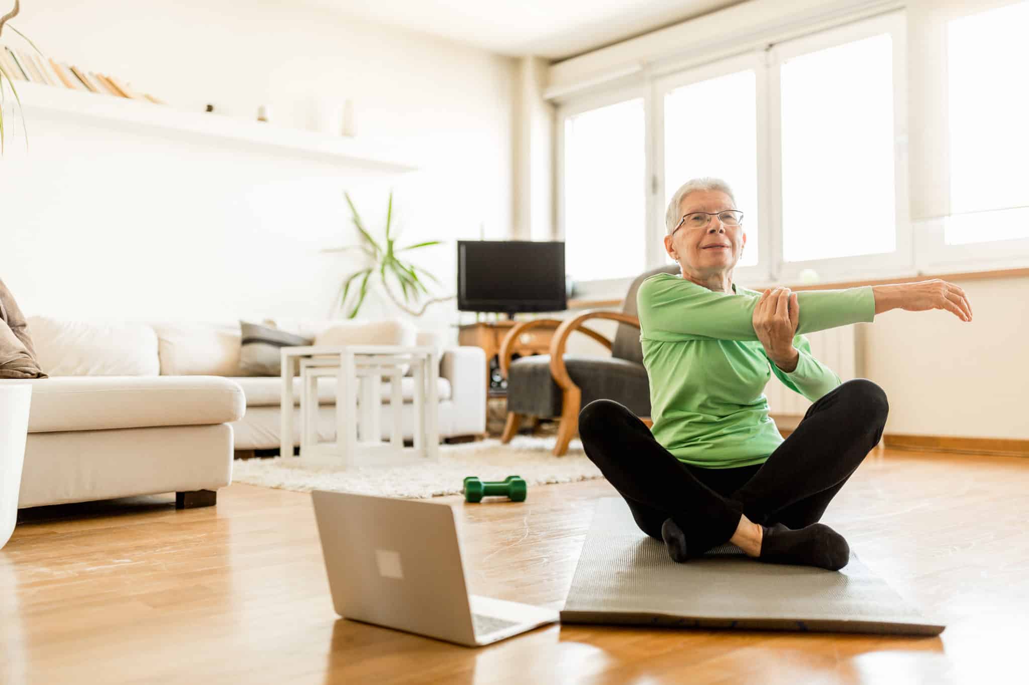 Active senior woman home exercising with online coach