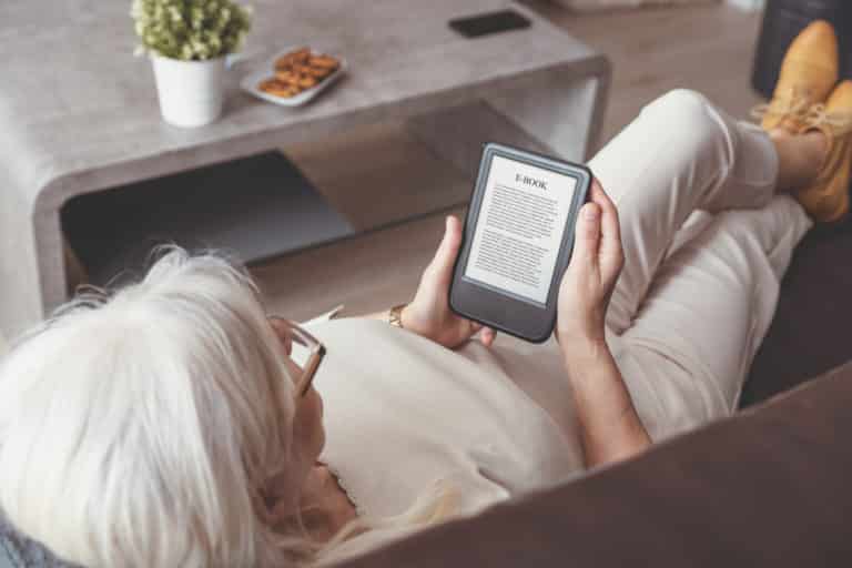 Woman sitting by the window, reading an e-book
