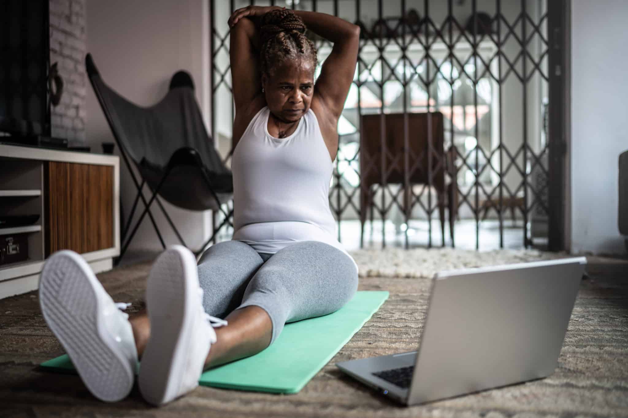Senior woman stretching doing exercise class with laptop at home