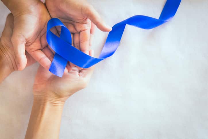 Hands holding deep blue ribbon on white fabric with copy space. Colorectal Cancer Awareness, Colon cancer of older person and world diabetes day, Child abuse prevention. Healthcare, insurance concept.