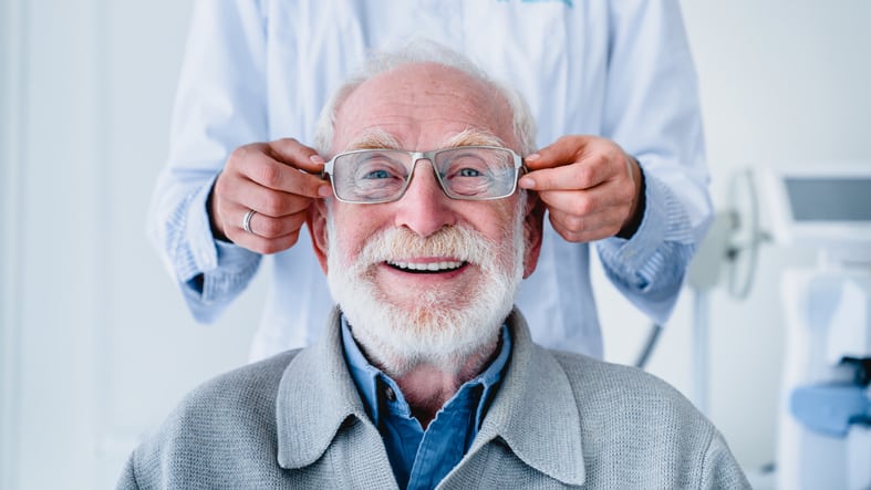 Doctor fitting glasses on cheerful aged male patient: cropped photo