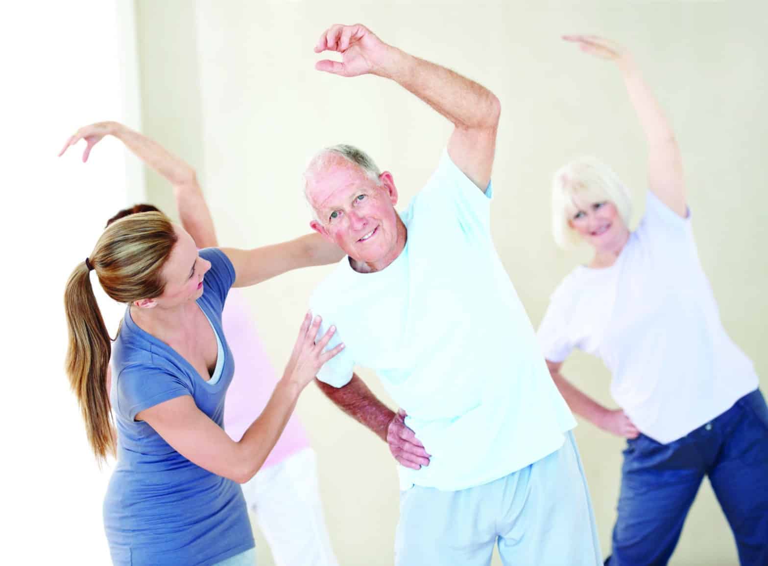 Portrait of an elderly man doing stretches and being assisted by a young instructor