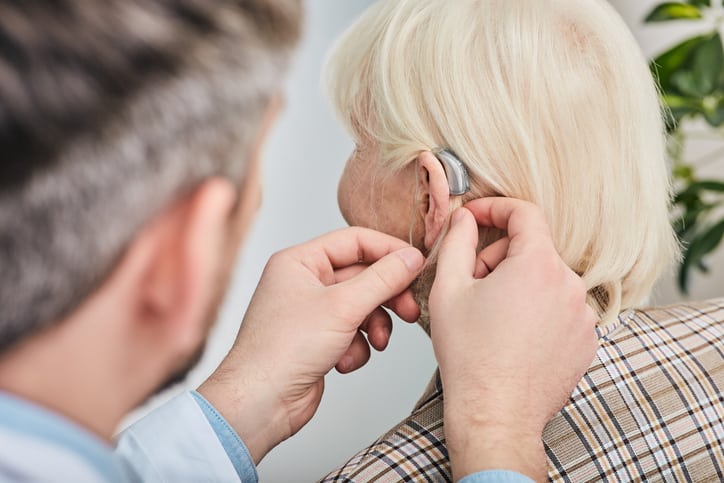 Audiologist inserting hearing aid on a senior woman's ear, close-up. Deafness treatment, hearing solution