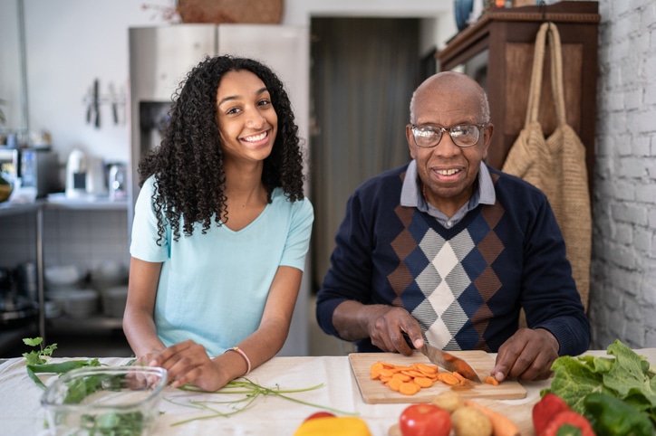 Portrait of happy girl with grandfather preparing vegetables at home